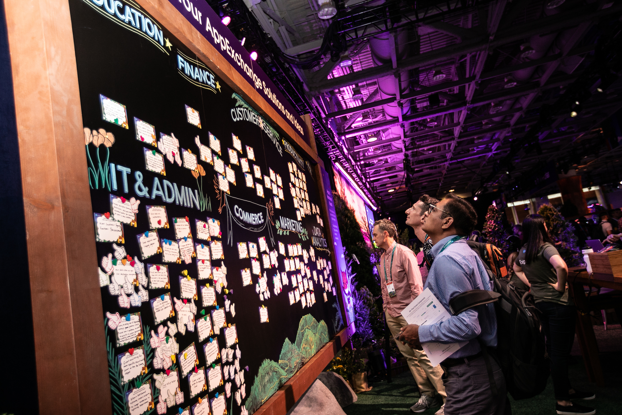 Several Dreamforce 22 attendees stand in front of and inspect the AppExchange idea board. 