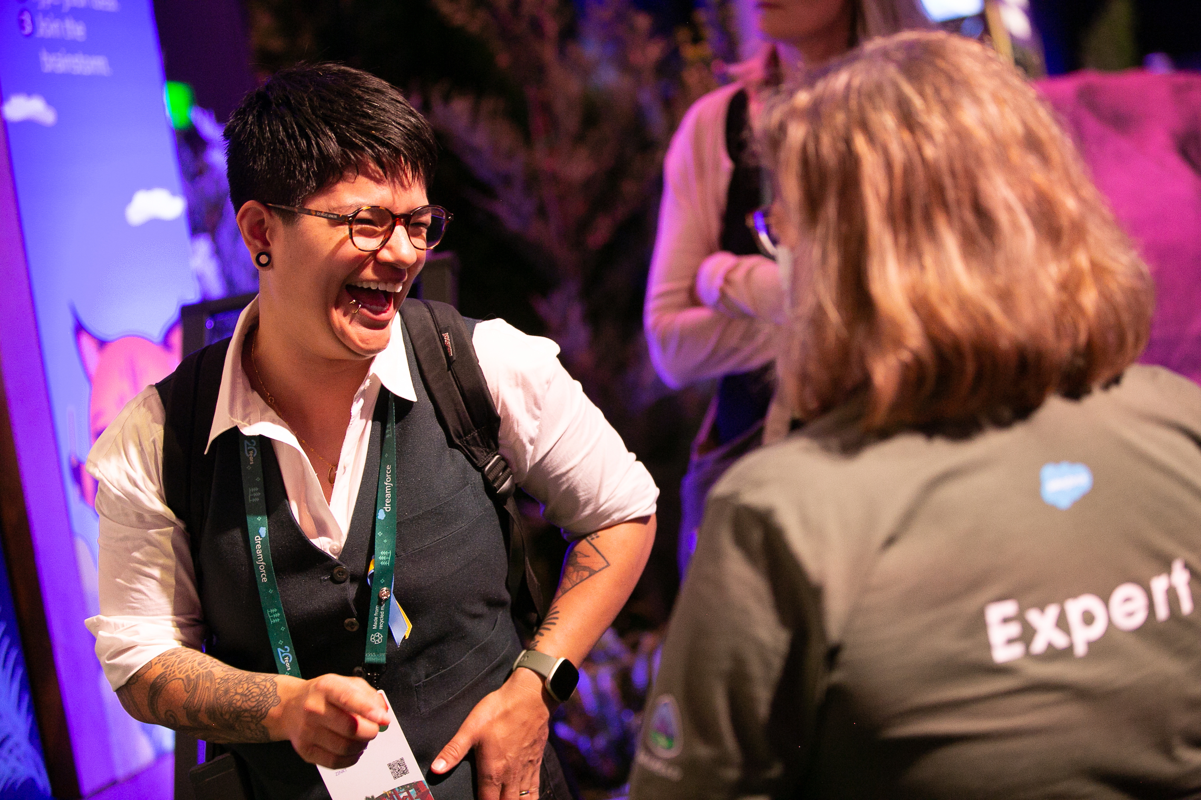 A person with short hair and glasses laughs with another attendee at Dreamforce22. 