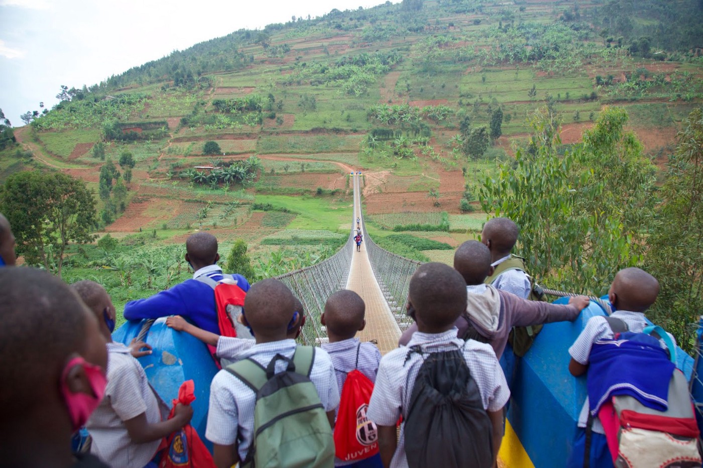 A group of young schoolchildren gather near a bridge in a rural setting. 