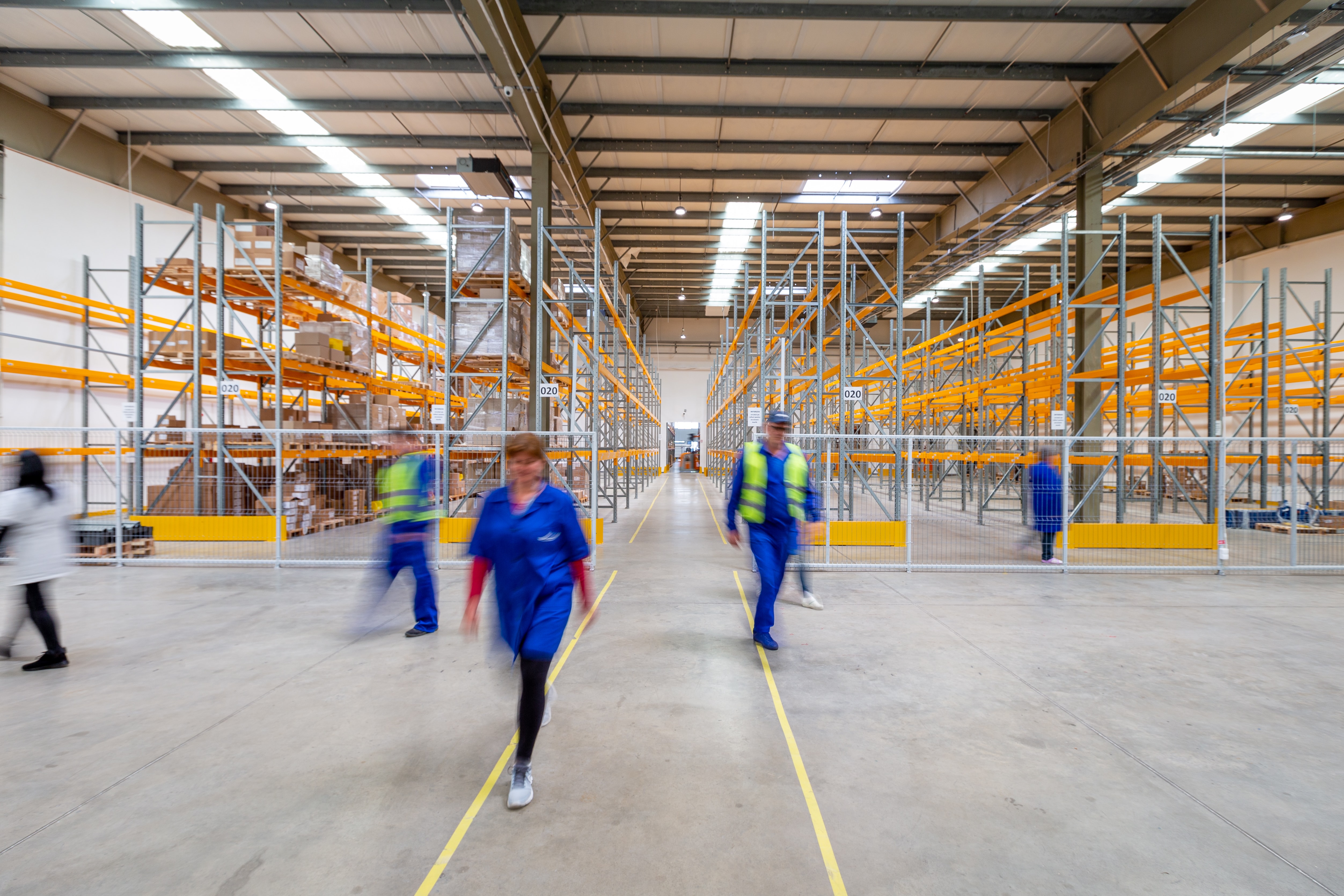 Workers wearing blue walk around a warehouse. 