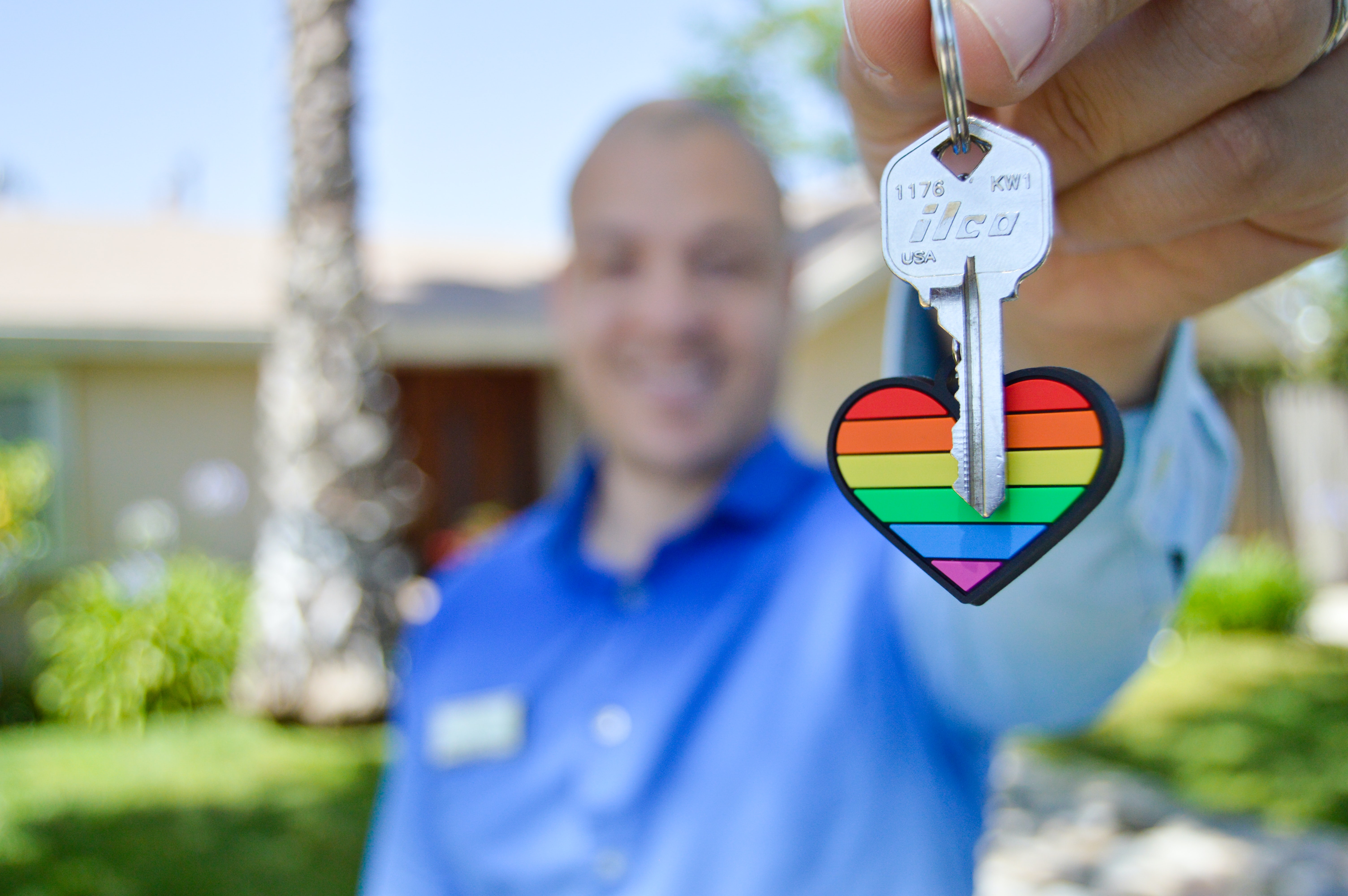A person holds a set of home keys with a rainbow keychain.
